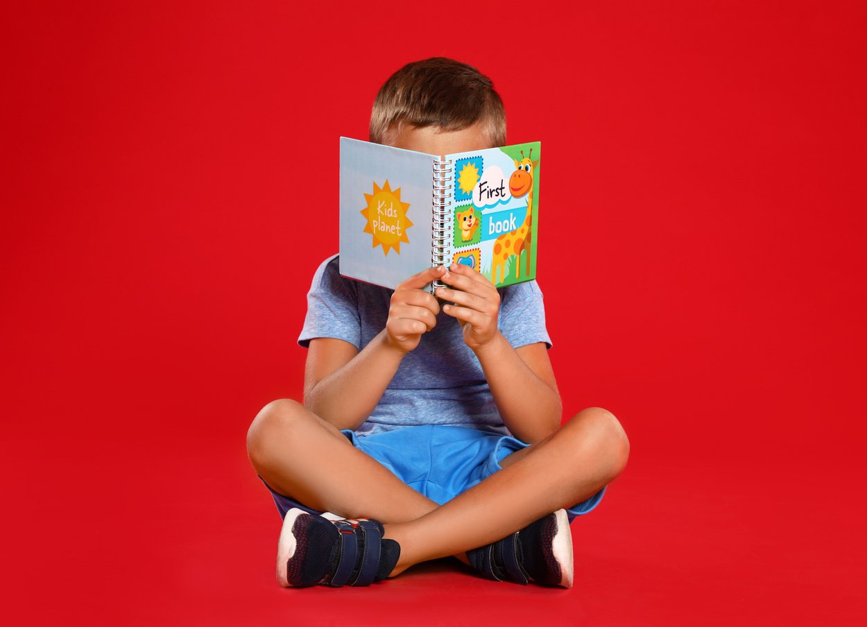 Cute Little Boy Reading Book on Red Background